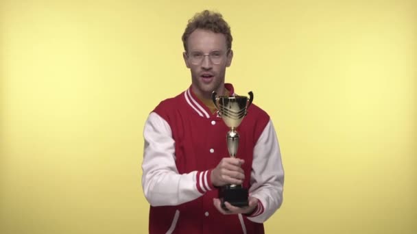 szczęśliwy młody człowiek w okularach trzyma złote trofeum na żółto - Materiał filmowy, wideo