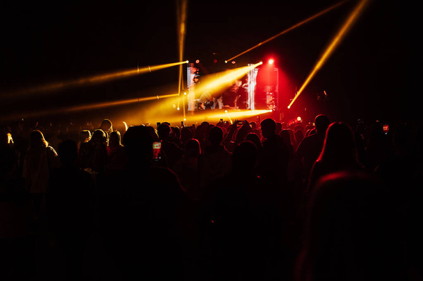 Szczęśliwi fani grupy muzycznej tańczą na koncercie. jasne światło reflektorów świeci na tysiące widzów - Zdjęcie, obraz
