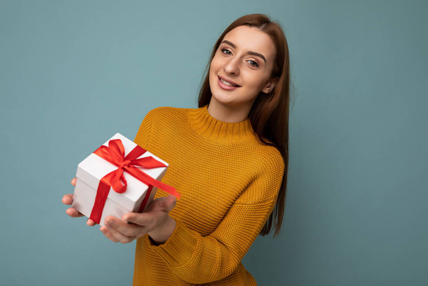 Shot of attractive positive smiling young brunette woman isolated over colourful background wall wearing everyday trendy outfit holding gift box and looking at camera - Photo, image