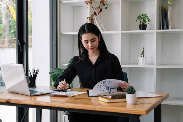 Portrait of Asian young female Businesswoman working on laptop computer doing finances,accounting analysis,report,data and pointing graph at the office - Фото, зображення
