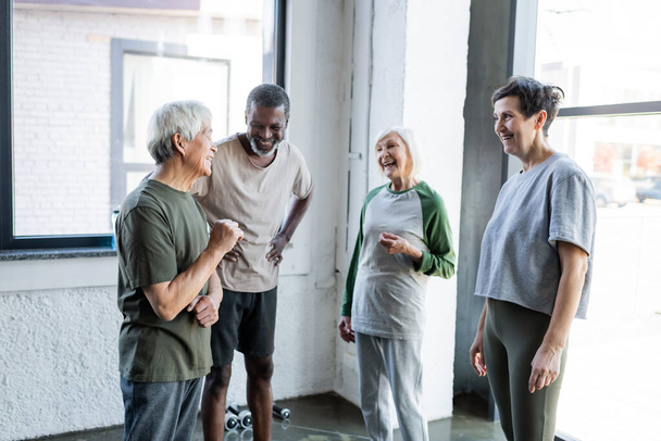 Positive interracial senior people in sportswear talking in gym  - Фото, зображення