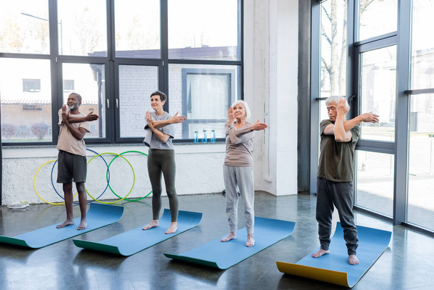 Monikulttuurinen vanhempi ihmiset harjoittelevat joogaa matot urheilukeskuksessa  - Valokuva, kuva