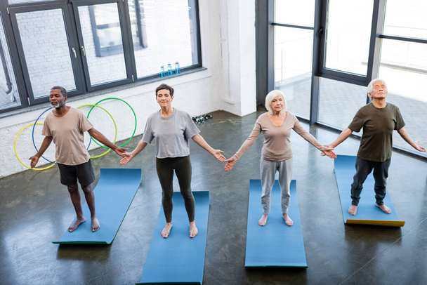 Vista ad alto angolo di persone anziane interrazziale in piedi in posa yoga nel centro sportivo  - Foto, immagini