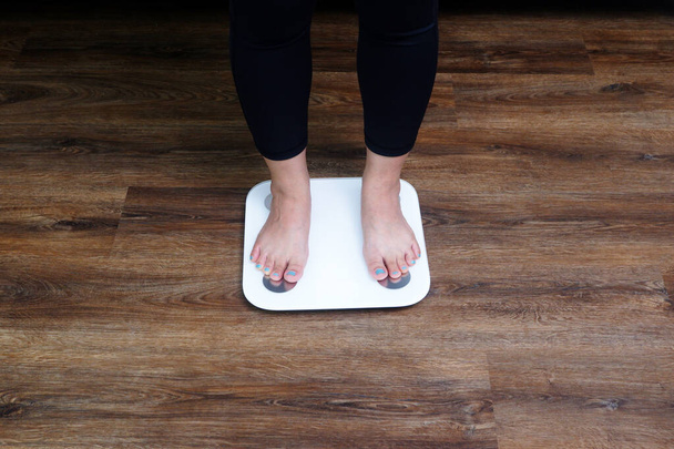Zbliżenie żeńskich stóp wkraczających na wagę ciała. Kontrola masy ciała, koncepcja odchudzania. - Zdjęcie, obraz