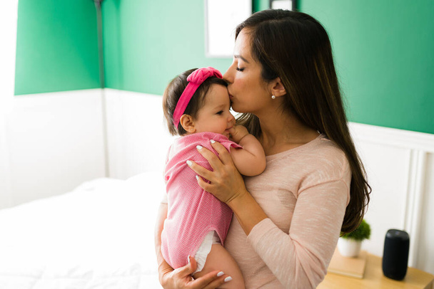 Я люблю свою малышку. Красивая молодая женщина целует лоб своей очаровательной маленькой дочери  - Фото, изображение