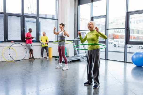 Happy elderly woman exercising with hula hoop on sports center  - Photo, Image