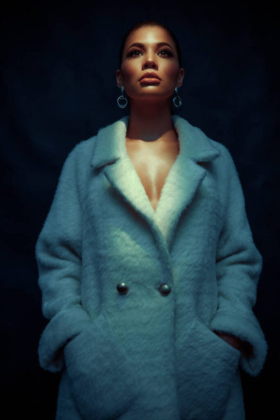 Portrait of an extraordinary beautiful stylish metis young woman with perfect smooth glowing mulatto skin, full lips and fashionable make up. Dark background. Studio shoot of an african american female model in fur coat  - Photo, Image