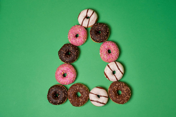 Пончики рожевого, коричневого та білого кольорів у формі трикутника на зеленому фоні
  - Фото, зображення