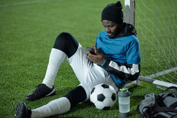 Młody, spokojny sportowiec przewijający się w smartfonie po treningu - Zdjęcie, obraz