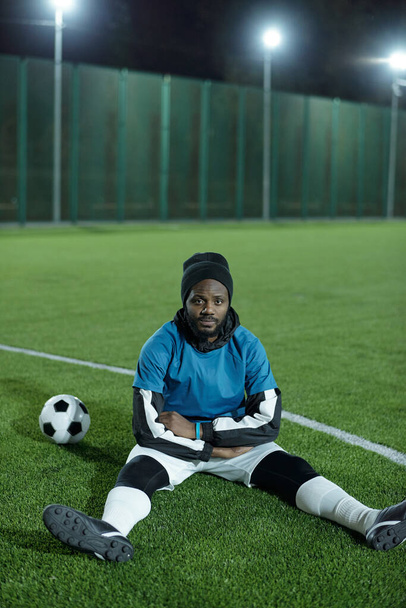 Junger erholsamer Mann afrikanischer Herkunft sitzt auf Fußballplatz - Foto, Bild