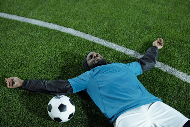 Fiatal, pihentető, egyenruhás sportoló, zöld gyepen fekszik - Fotó, kép