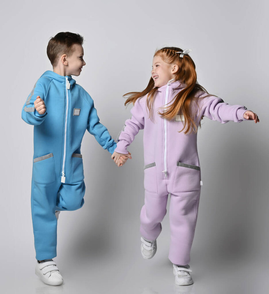Playful frolic kids boy and girl in blue and pink jumpsuits with are running together looking at each other - Фото, изображение