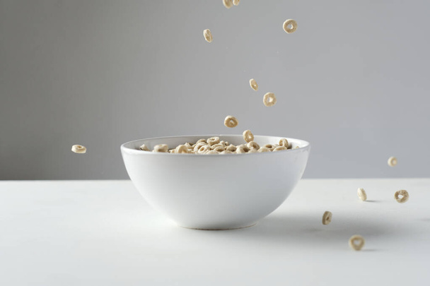 Loop cereais caindo em uma tigela branca em uma mesa branca com fundo cinza - Foto, Imagem