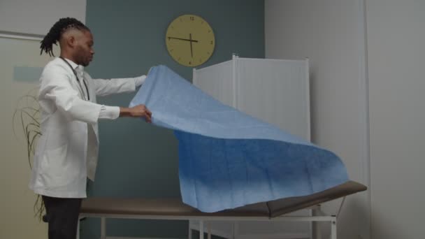 Mieslääkäri tai sairaanhoitaja, joka peittää diagnostisen sängyn uudella levyllä sisätiloissa - Materiaali, video