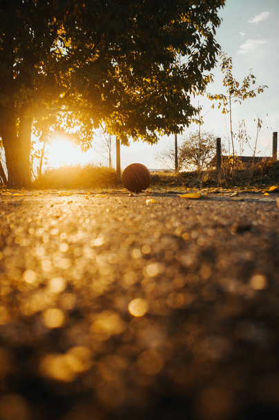 A vertical shot of a basketball on the pavement at sunset - Fotografie, Obrázek