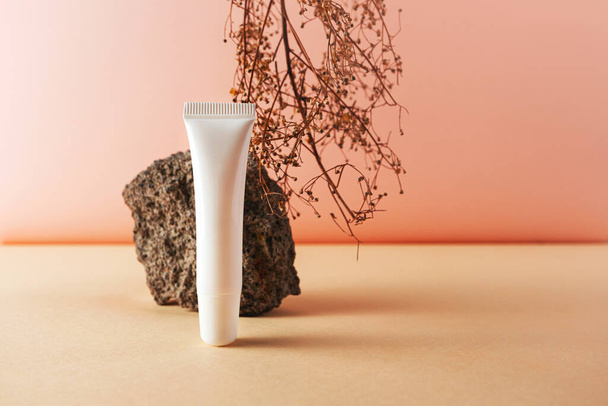 Tubo de plástico blanco y piedra y hierba seca natural fotografía cosmética creativa bodegón. Bálsamo labial en blanco maqueta vacía - Foto, imagen