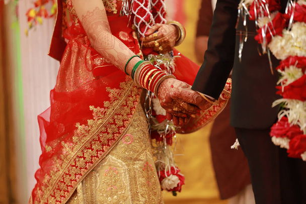 A closeup of the groom and the bride holding hands during a traditional Indian wedding - 写真・画像