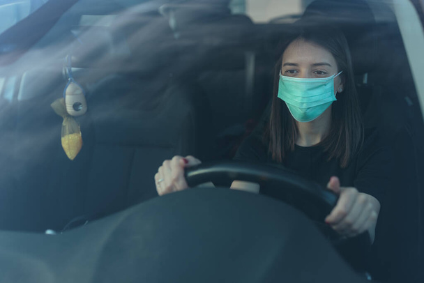 A Caucasian female in a face mask driving a car - 写真・画像