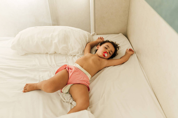 Cute little girl with a pacifier sleeping comfortably in a bed. - Foto, afbeelding