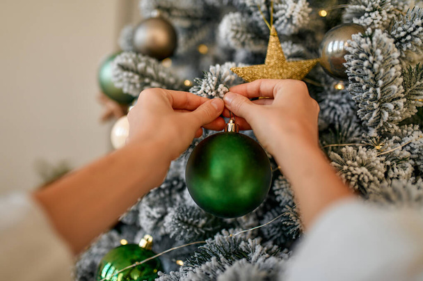 Merry Christmas and Happy New Year! Women's hands decorate a snow-covered Christmas tree with balls and toys. - Foto, afbeelding