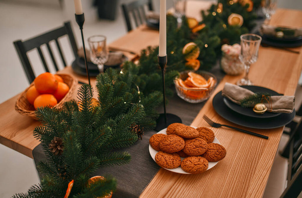 Veselé Vánoce a šťastný nový rok! Připravuje se na slavnostní večeři. Nastavení stolů a dekorace se svíčkami, smrkovými větvemi a sušenými oranžovými klíny. - Fotografie, Obrázek