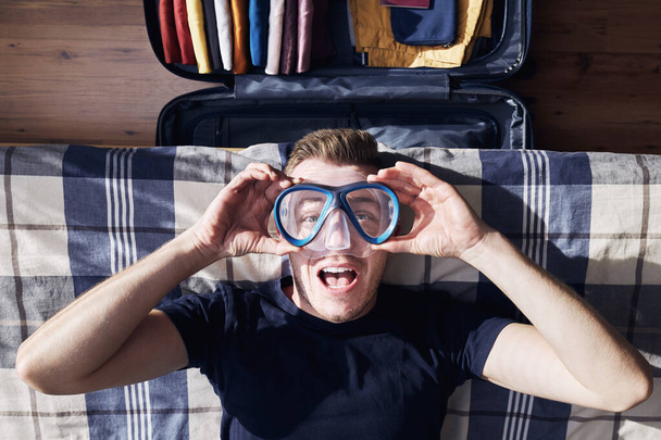 Crazy portrait of happy young man during packing suitcase and planning travel adventure - Фото, изображение
