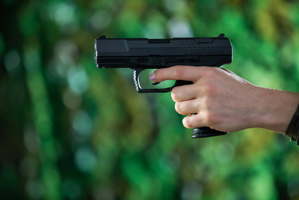 A woman holds a gun in her left hand. Close-up view. - Φωτογραφία, εικόνα