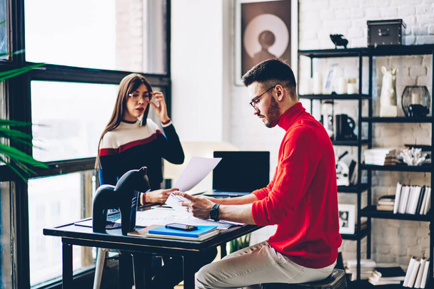Skilled male and female partners collaborating on paperwork using laptop computer in loft coworking space, Caucasian hipster guys analyzing information from education reports brainstorming together - Photo, image