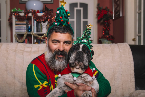 Porträt eines bärtigen Mannes auf dem Sofa und seiner französischen Bulldogge zu Weihnachten - Foto, Bild