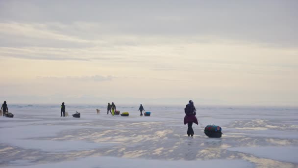 Fila de turistas con trineos equipados a pie sobre hielo congelado a horizonte brumoso - Imágenes, Vídeo