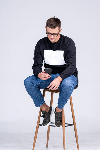 Young student in eyeglasses in lifestyle casual cloth. Handsome clever man sitiing on the stool in studio. - Foto, Imagem