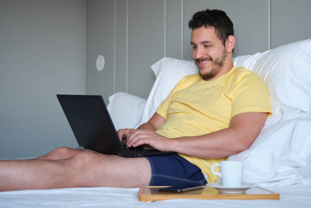 Uomo che lavora con il computer portatile in un letto in camera d'albergo. - Foto, immagini