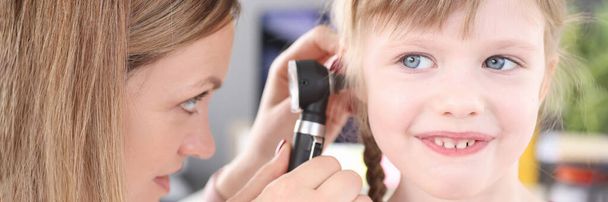 Оториноларинголог проводит медицинское обследование уха маленькой девочки - Фото, изображение