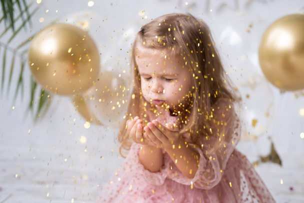 happy child girl with long hair in pink dress blowing confetti and celebrating her birthday - 写真・画像
