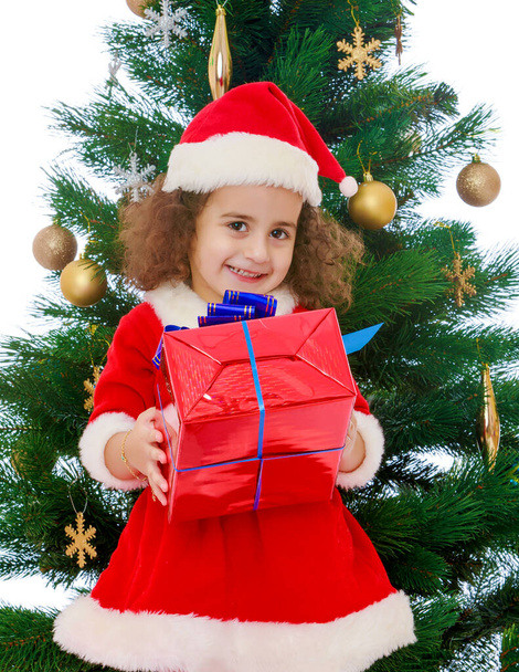 Klein meisje in de buurt van de kerstboom met een geschenk in zijn handen - Foto, afbeelding