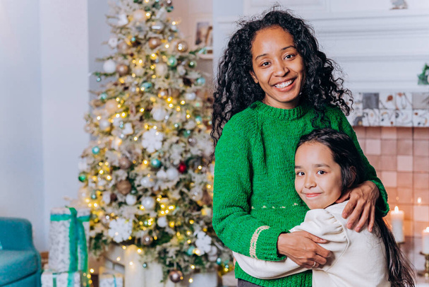 Mamá y su hija se abrazan de pie contra el árbol de Navidad - Foto, Imagen