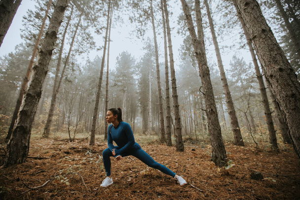 Csinos fiatal nő kék melegítőben nyújtózkodik edzés előtt az őszi erdőben - Fotó, kép