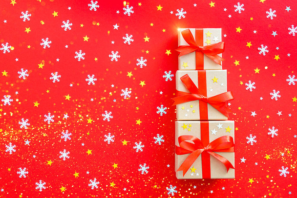 Three beautiful gifts are decorated with a ribbon. On a red background with gold and silver stars and snowflakes. Postcard for Christmas and New Year. - Foto, Imagem