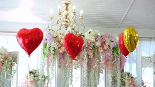 διακόσμηση της αίθουσας δεξιώσεων με λευκά τεχνητά λουλούδια και κόκκινα μπαλόνια σε σχήμα καρδιάς - Πλάνα, βίντεο