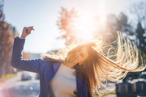 Portrait of a young happy woman in the city in the sunny rays with flying hair - 写真・画像
