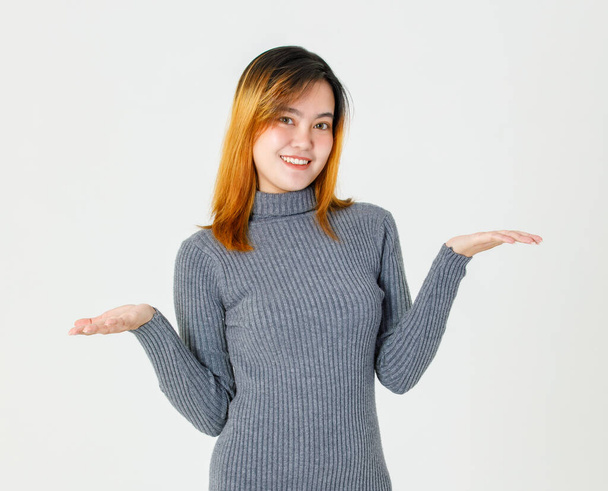 Portrét close up studio záběr asijské mladé teen žena modelu v šedém roláku svetr stojící s úsměvem drží prázdné ruce nahoru prezentující reklamní výběr produktu možnost na bílém pozadí. - Fotografie, Obrázek