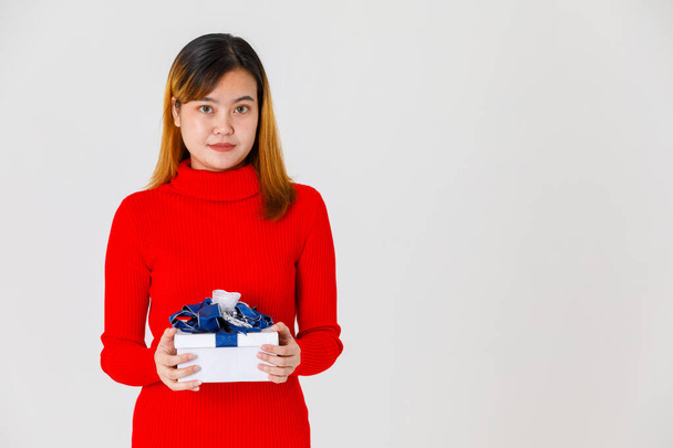 Portrait studio shot of Asian young happy female birthday girl in red long sleeve sweater dress holding gift present box with blue silver ribbon in hands celebrating important day on white background. - Photo, Image