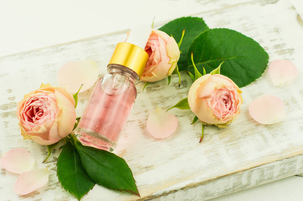 extrat of rose petals in a glass cosmetic bottle against the background of a rose bud and a white podium. anti-aging facial care - Foto, afbeelding