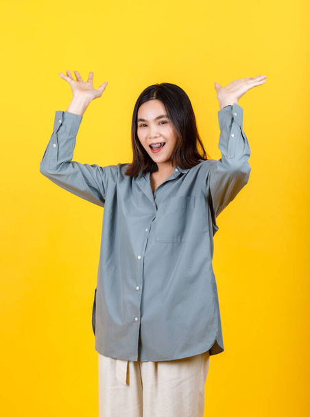 Жива азіатка на сорочці з довгим рукавом користується ізольованим портретом жіночого одягу, піднімаючи руку, посміхаючись, жестикулюючи, як мати несподівану можливість вище і щасливо пропонуючи привабливе просування - Фото, зображення