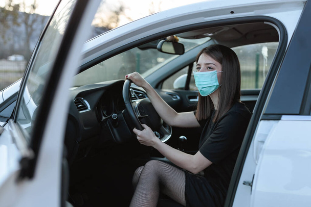 A Caucasian female in a face mask sitting in a car with an open door - Fotografie, Obrázek