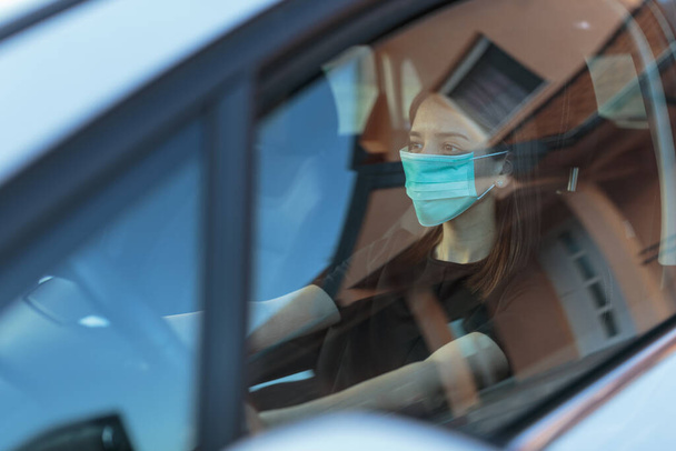 A Caucasian female in a face mask driving a car - Фото, зображення