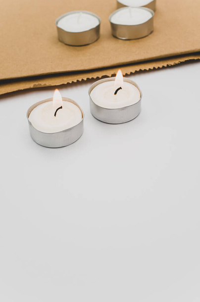 row of white scented wax tea lights on a white tabletop with copy space and folded paper bag - Φωτογραφία, εικόνα