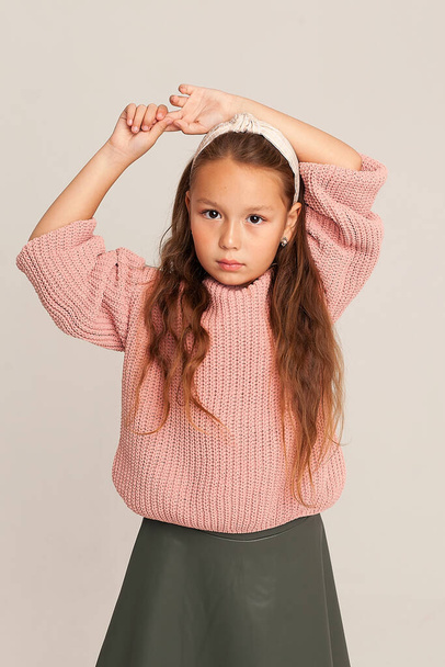 A close-up portrait of a serious little beautiful girl with long hair, the child looks at the camera with a serious look and raised her hands above her head. stylish portrait of a child. - Foto, Imagem