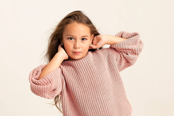 A close-up portrait of a serious little beautiful girl with long hair, the child looks at the camera with a serious look and raised her hands above her head. stylish portrait of a child. - Photo, Image