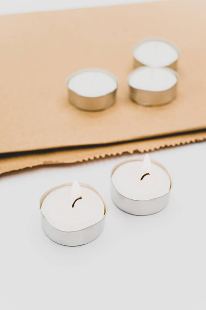 row of white scented wax tea lights on a white tabletop with copy space and folded paper bag - Photo, Image